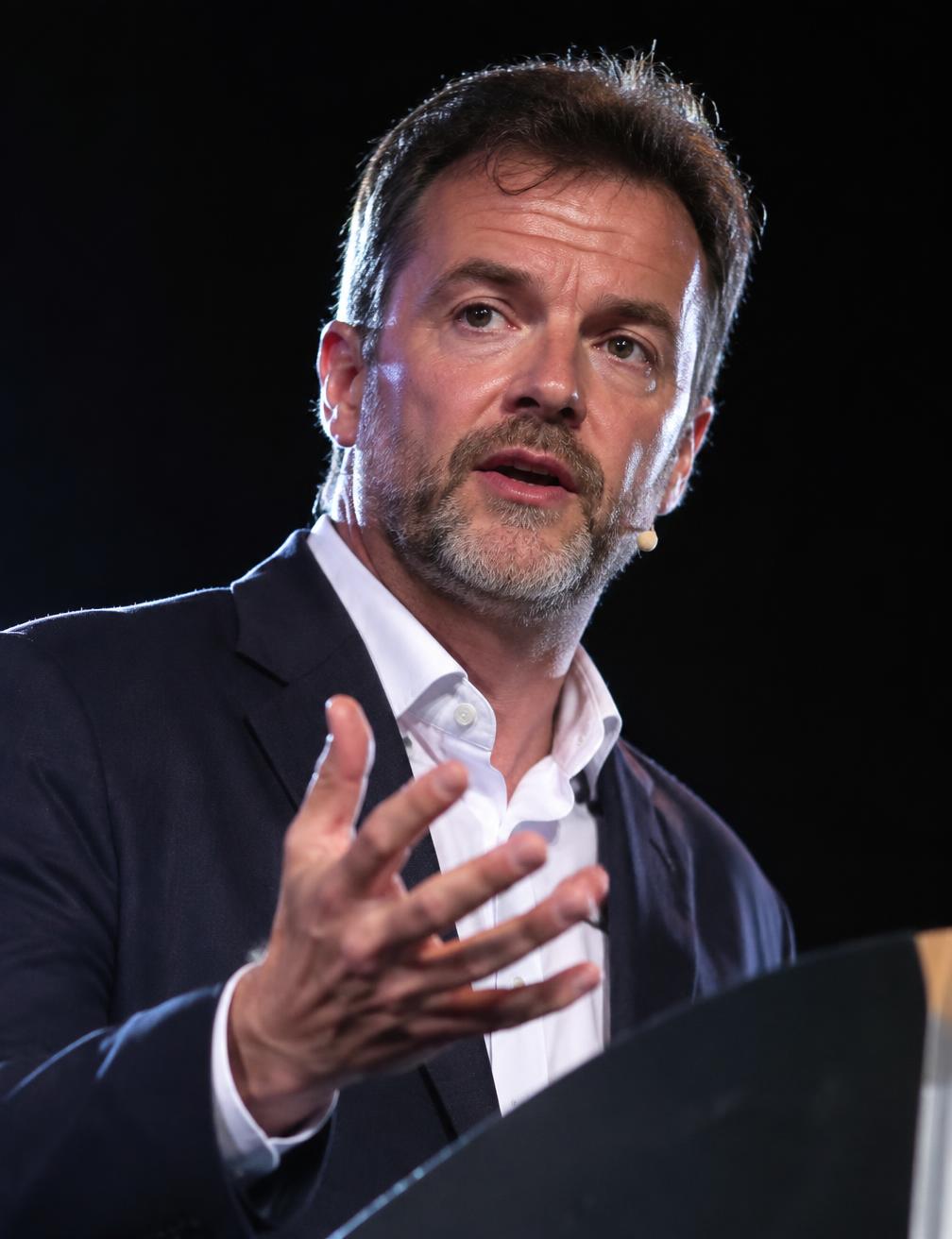 Close portrait of a keynote speaker gesturing at a podium under dramatic light